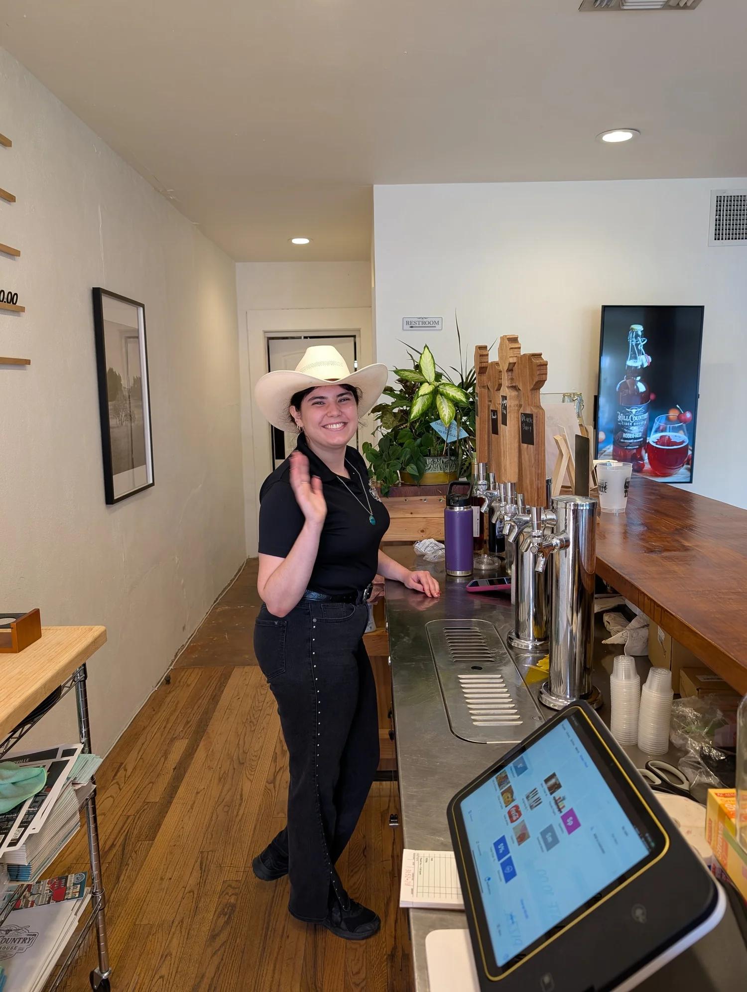 A smiling host in a white cowboy hat behind the bar